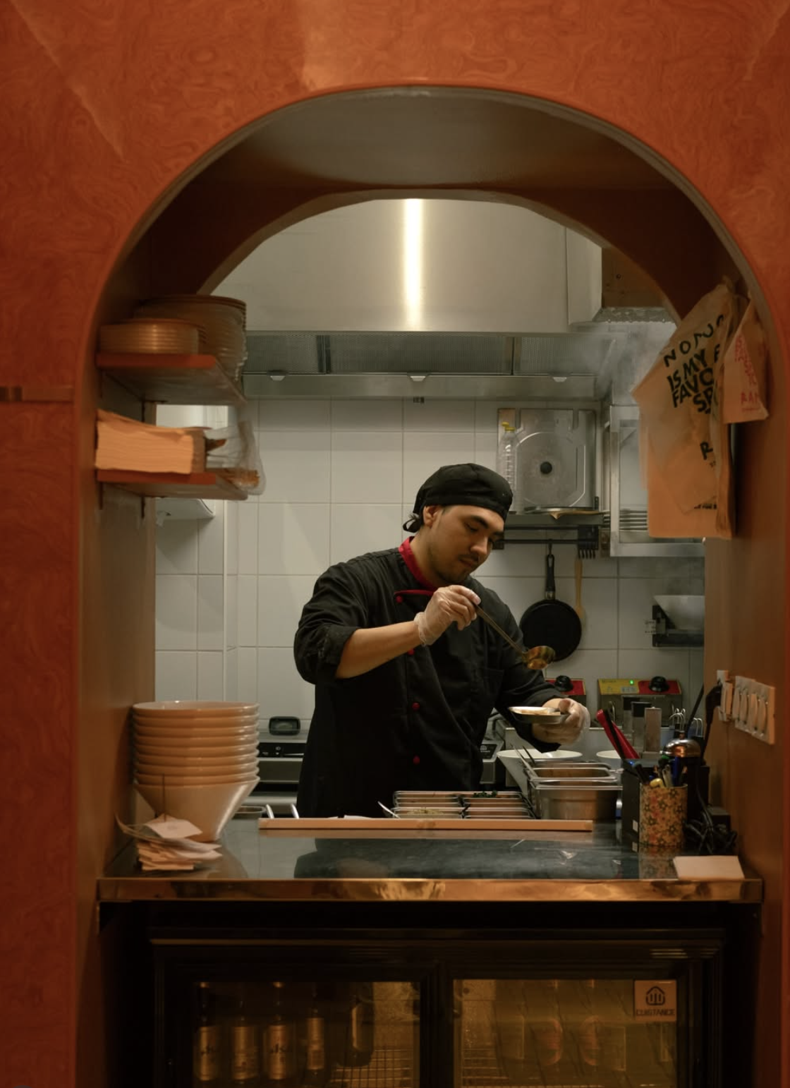 Le chef Nodoo dressant un bol de ramen derrière l'arche de la cuisine